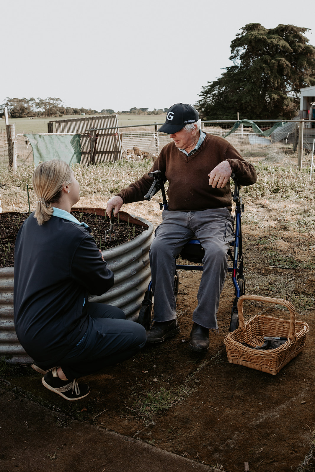 Nurse supporting elderly man in wheelchair with gardening activity at home in Portland, Victoria.