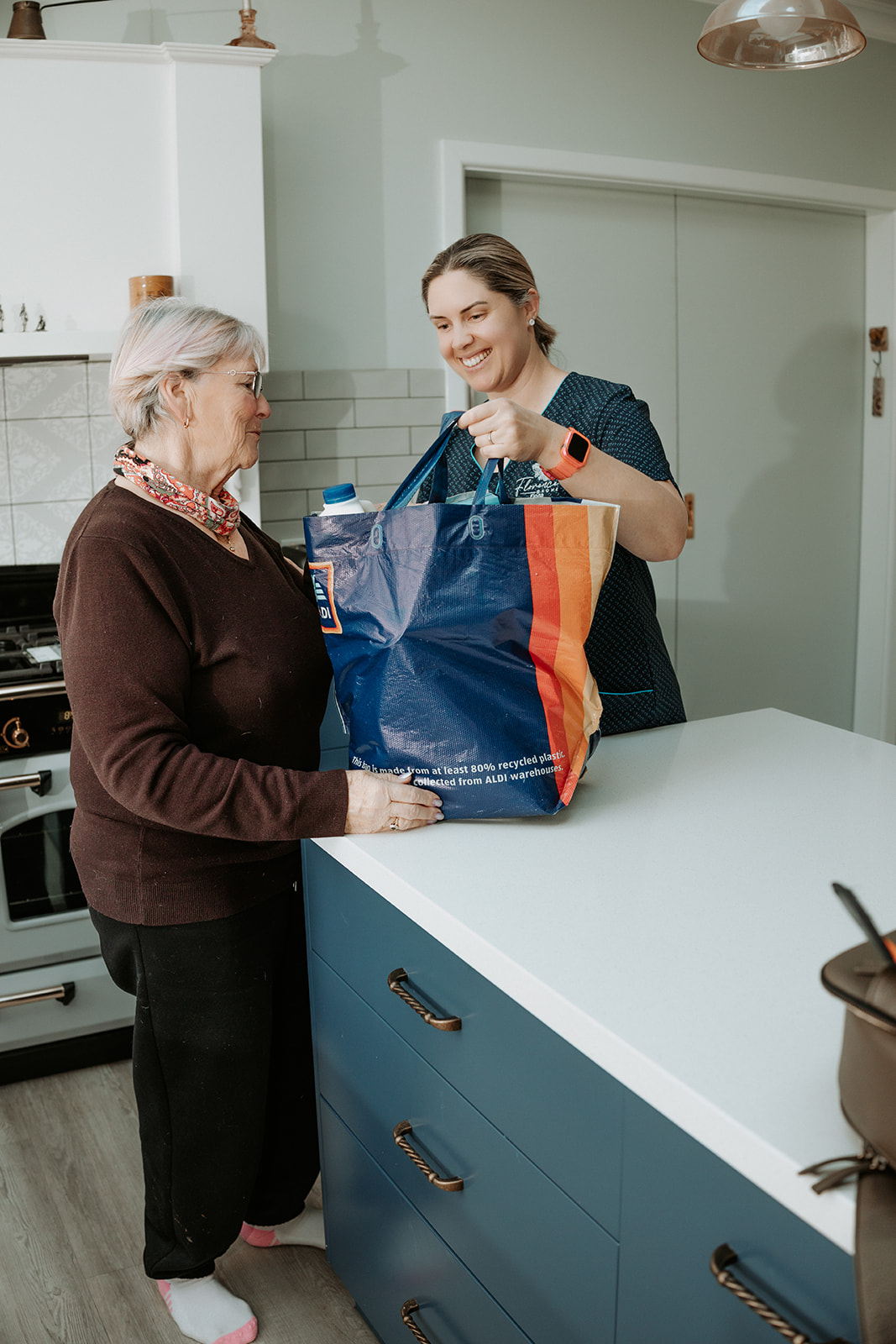 Nurse supporting elderly woman at home with groceries in Portland, Victoria.