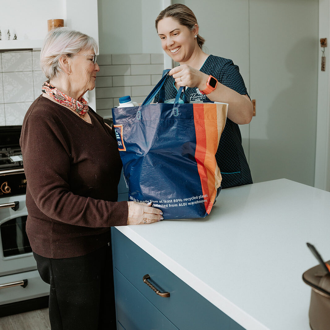 Nurse supporting elderly woman at home with groceries in Portland, Victoria.